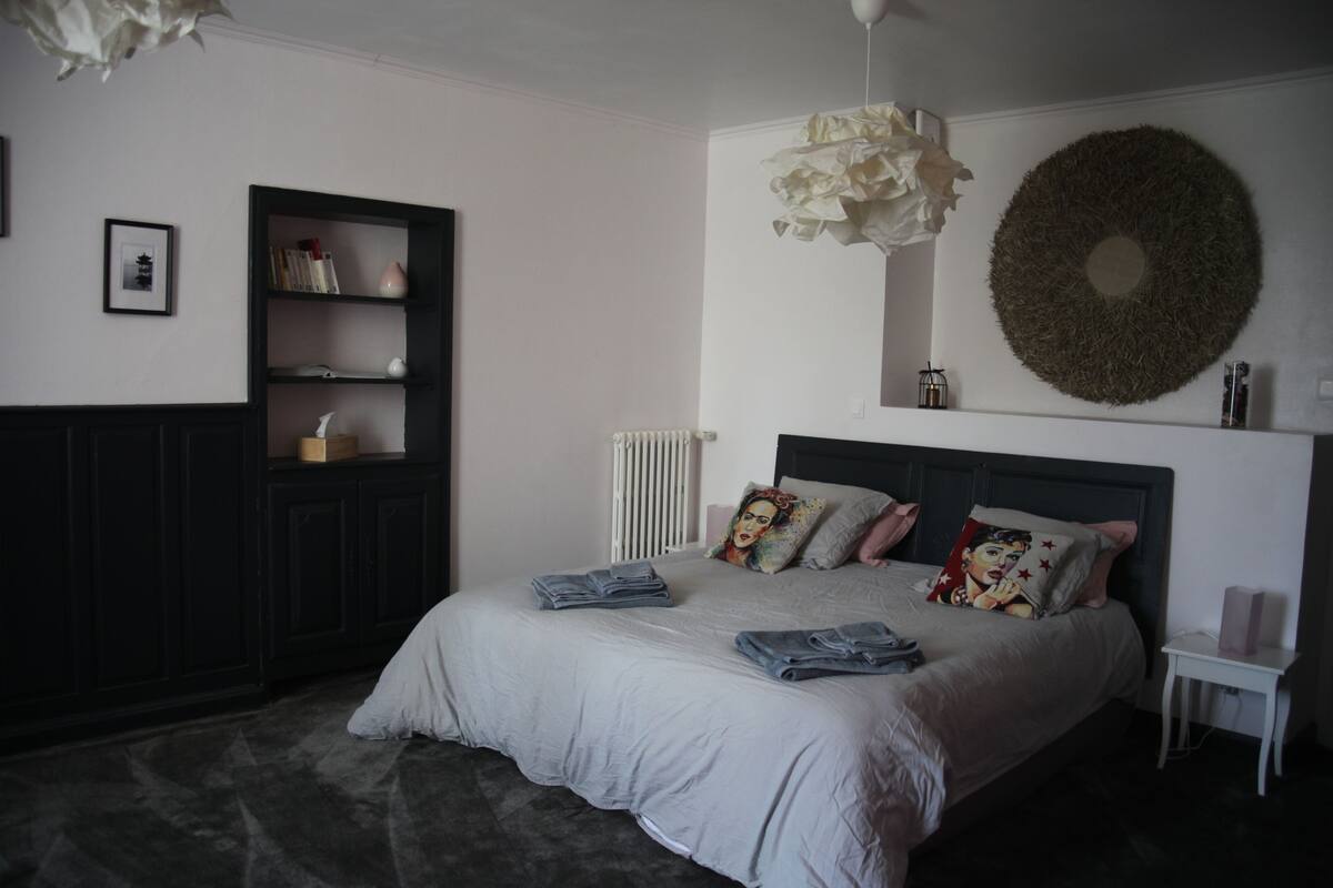 Ein Schlafzimmer mit einem Bett, einem Kleiderschrank, einem Heizkörper, einem an der Wand befestigten Kranz und einem kleinen weißen Nachttisch.