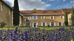 A stone building with multiple windows and shutters, surrounded by a field of purple flowers. - Le Clos Ayanna (Crémieu)