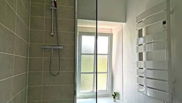 Un baño con ducha, ventana y estante empotrado.
