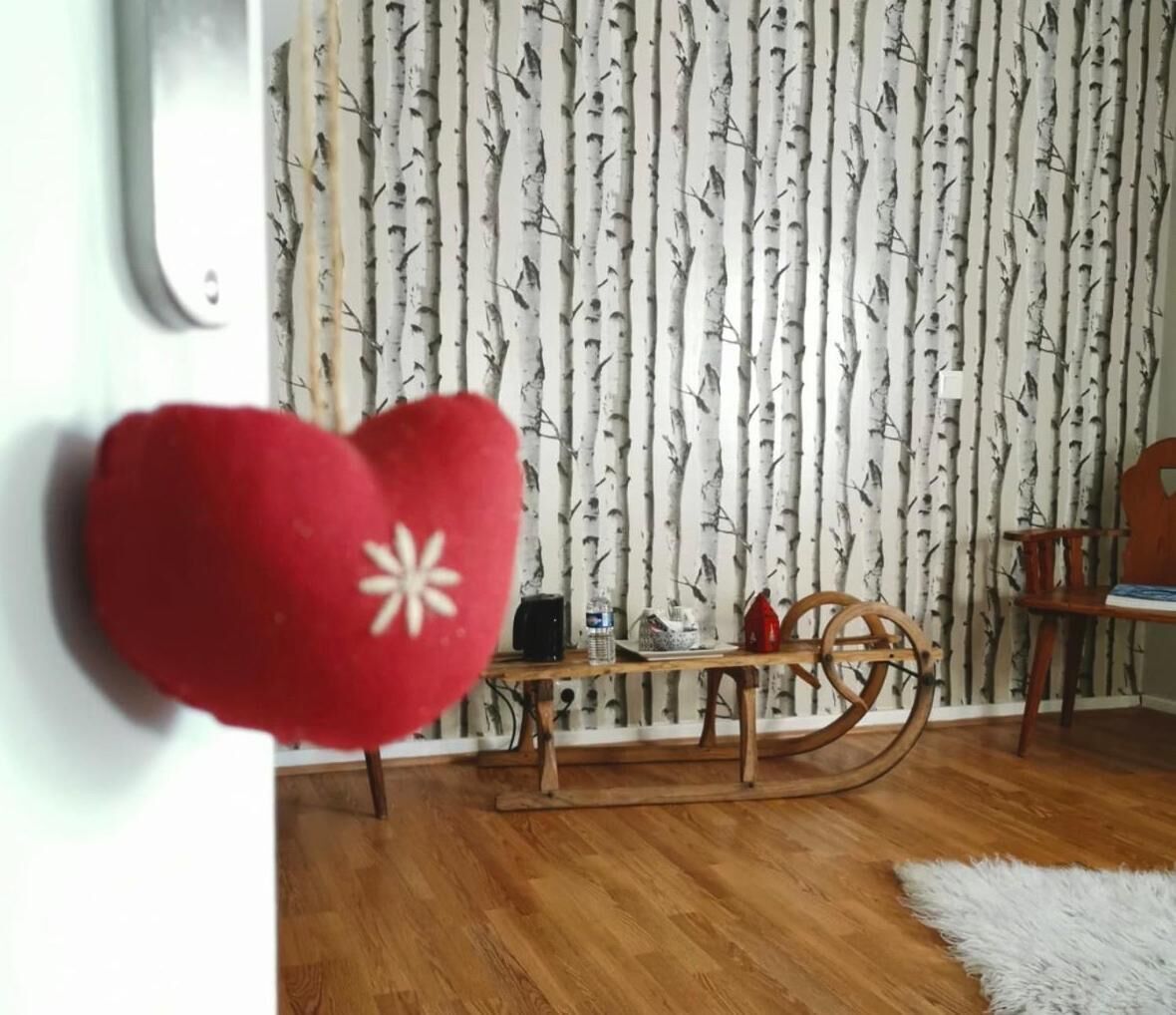 Une pièce avec un papier peint à motifs de bouleau, une table en bois sur laquelle se trouve une bouilloire, un objet rouge en forme de cœur et un tapis blanc et moelleux.