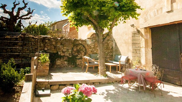 A courtyard with a stone wall, a tree, outdoor furniture, and a potted plant. - La Calade (Montouliers)
