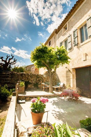 A courtyard with a stone wall, a tree, outdoor furniture, and a potted plant. - La Calade (Montouliers)