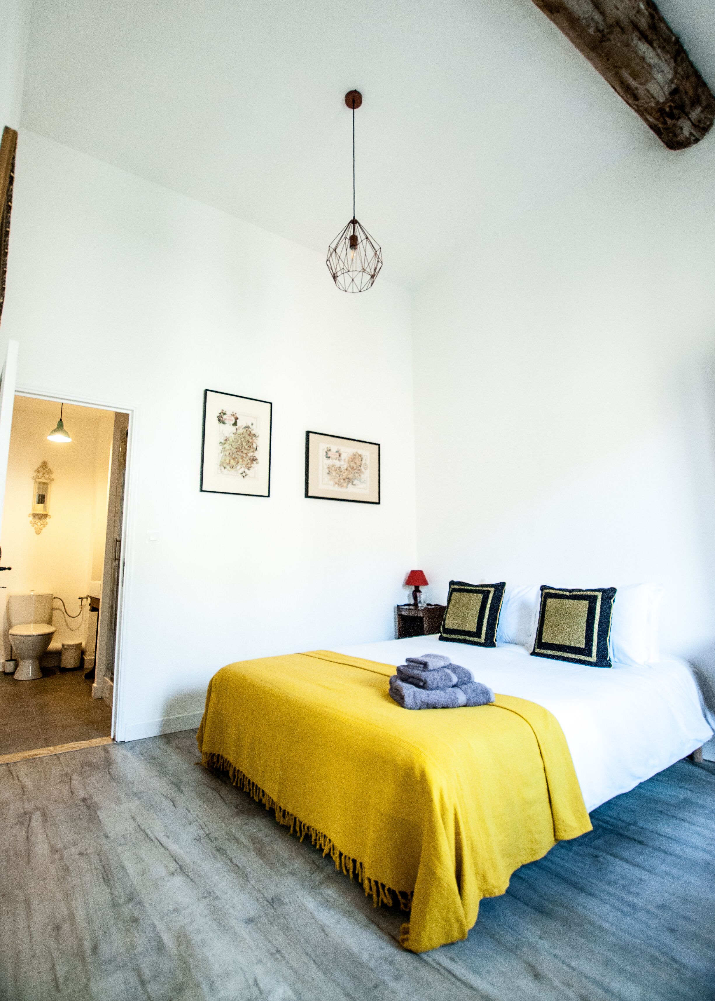 Een slaapkamer met een bed, een hanglamp en twee afbeeldingen in lijsten aan de muur.