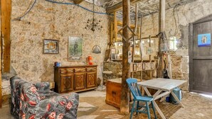 A rustic room with a stone wall, a wooden cabinet, a blue chair, and a table. - La Calade (Montouliers)