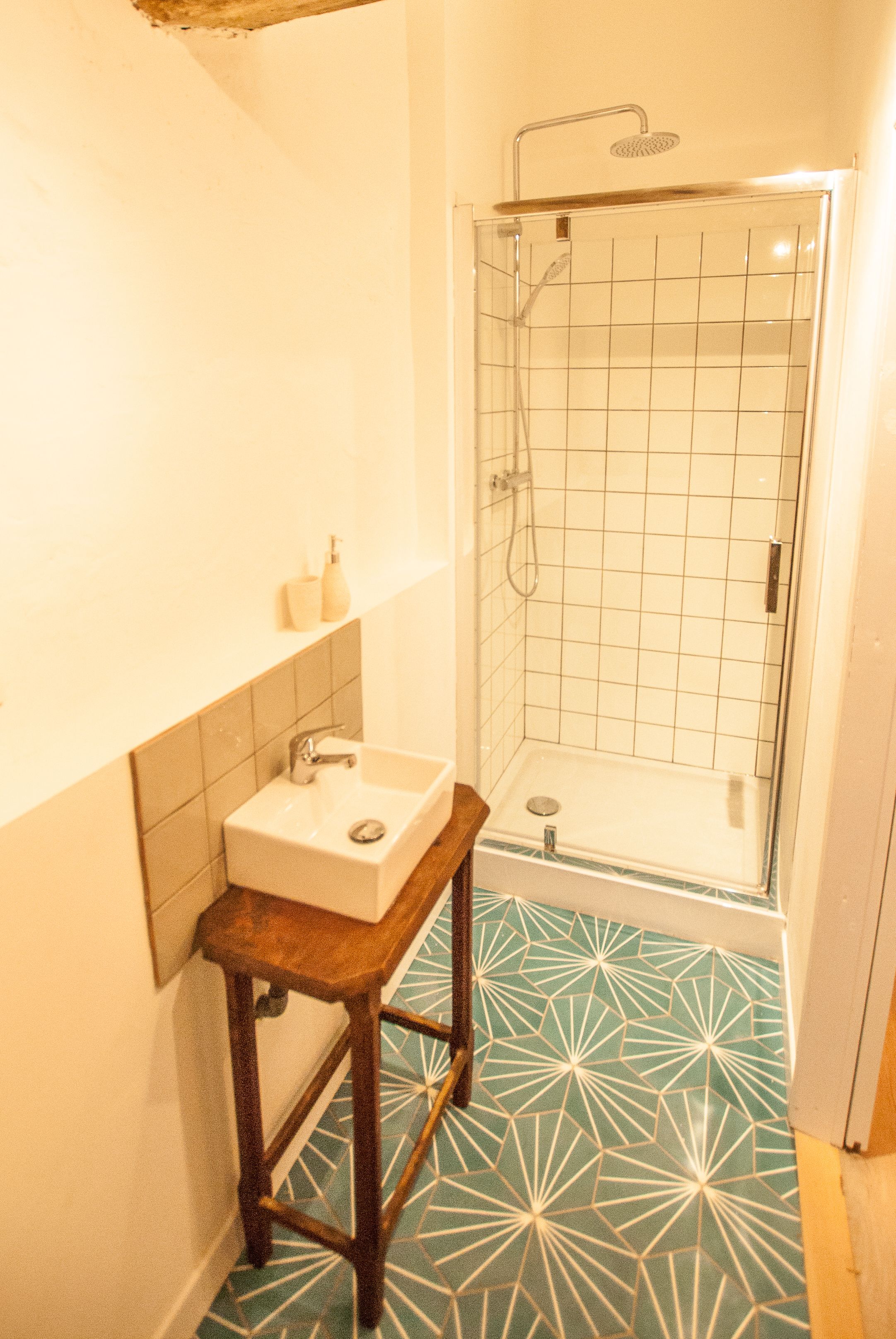 A bathroom with a sink, a shower, and a patterned floor.