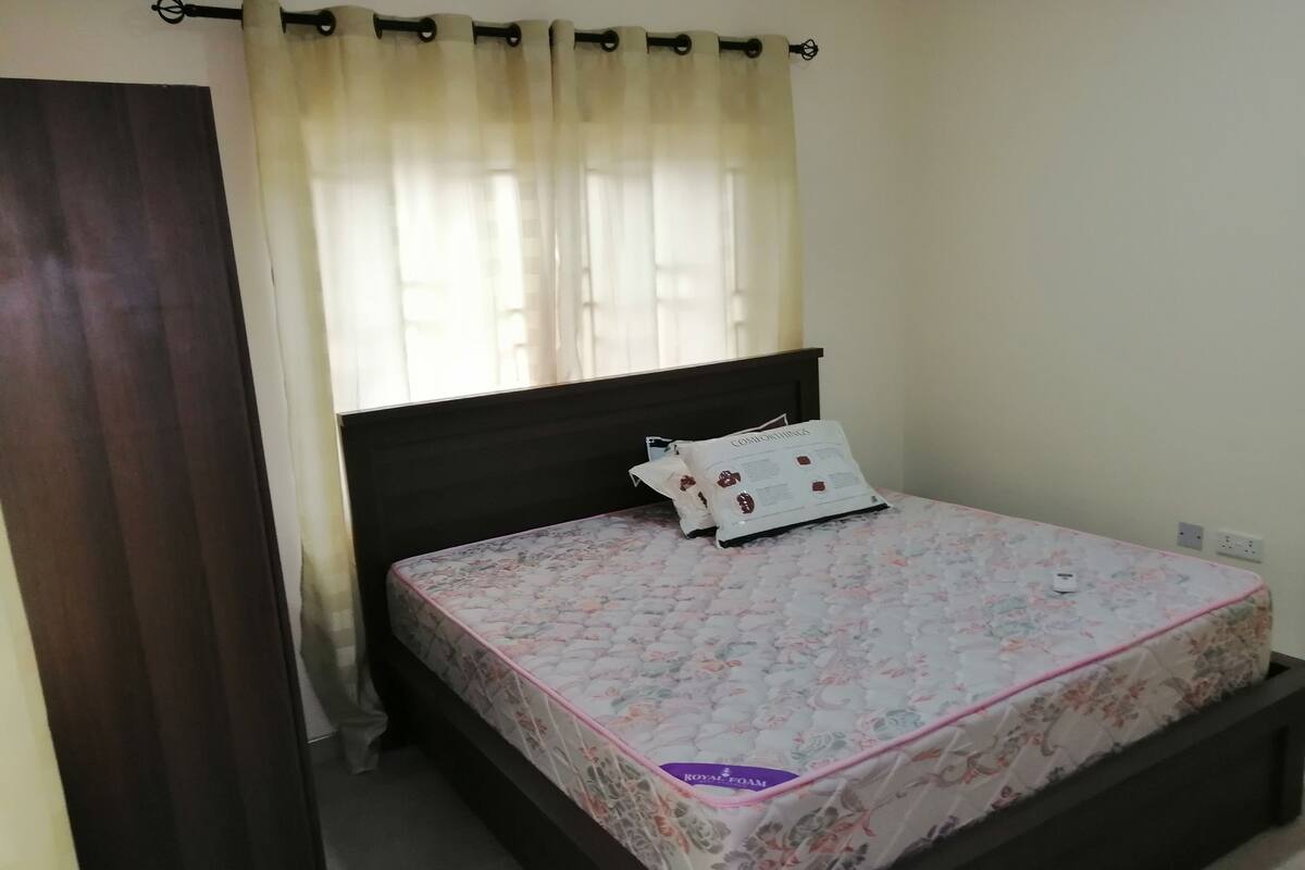 A bedroom with a bed, a window with curtains, and a bedside table.