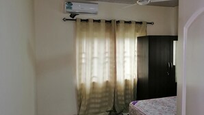 A room with a ceiling fan, an air conditioning unit, a bed with a patterned bedspread, and a dark-colored wardrobe. - Salomey Plaza (Kwabenya)