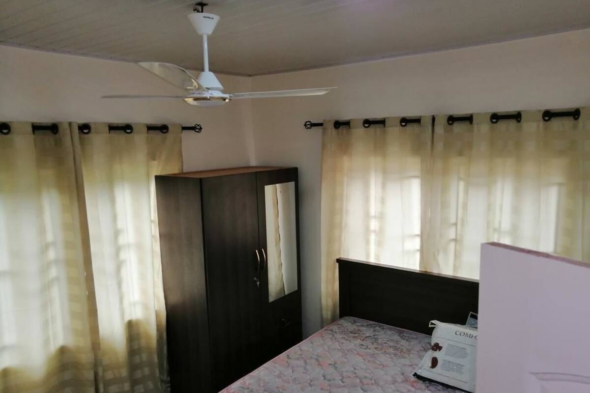 A bedroom with a bed, a wardrobe, a ceiling fan, and curtains.