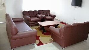A living room with a sofa set, a coffee table, and a TV mounted on the wall. - Salomey Plaza (Kwabenya)