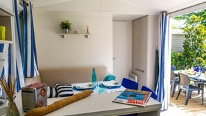 Un comedor con una mesa preparada para dos, una hogaza de pan y una revista sobre la mesa. Se observa una estantería con una planta y una pequeña estatua encima de la mesa.