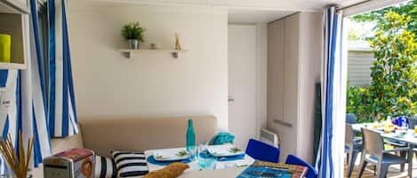 A dining area with a table set for two, a loaf of bread, and a magazine on the table. There is a shelf with a plant and a small statue above the table.
