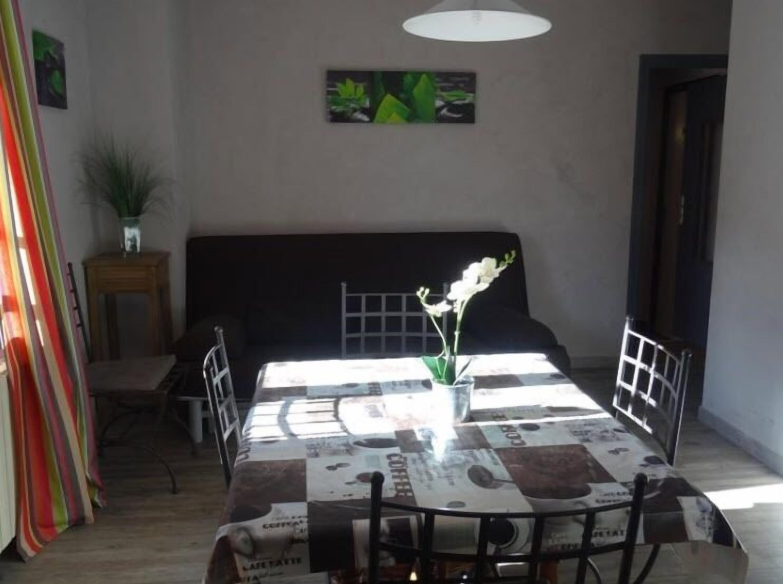 Un coin repas avec une table recouverte de journaux, une plante en pot et un canapé noir.