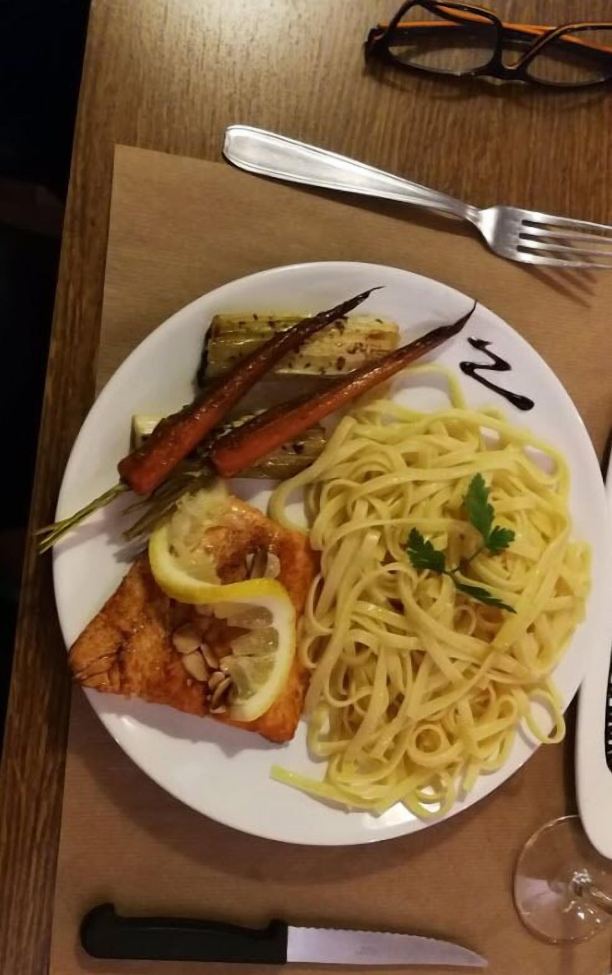 A plate of spaghetti with lemon slices and herbs, a piece of bread with lemon, and grilled vegetables.