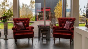 A modern interior with two red velvet armchairs, a small table, and a view of a building outside. - Hrafntinna Villa (Selfoss)