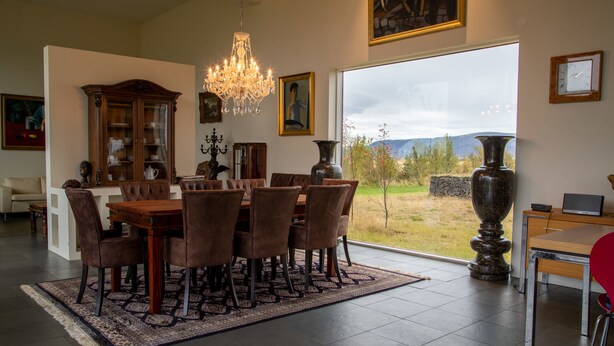 A dining area with a large table, chairs, and a chandelier. There is a view of a landscape through a large window. - Hrafntinna Villa (Selfoss)