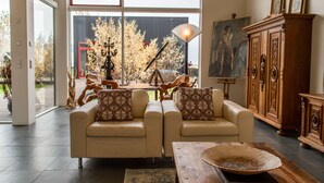 A modern living room with two sofas, a wooden cabinet, and a large window with a view of trees and a building. - Hrafntinna Villa (Selfoss)