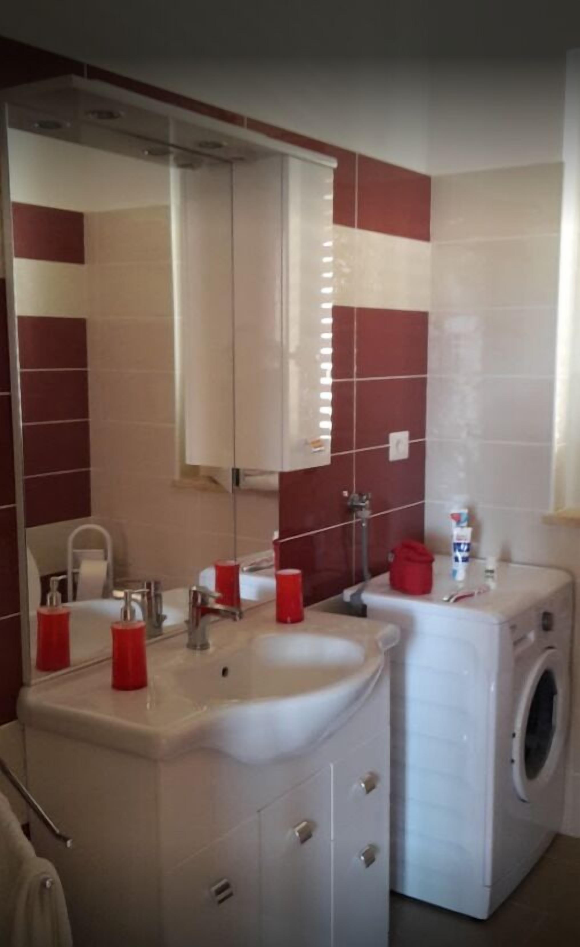 Casa de banho com lavatório, espelho, dosadores de sabonete vermelhos e máquina de lavar roupa.