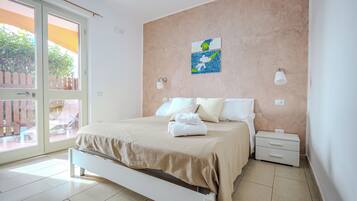 Un dormitorio con cama, mesita de noche, lámpara de pared y ventana con vista a un patio exterior.