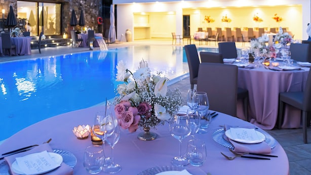 A poolside dining area with tables set for a meal, surrounded by a pool and a building with a stone facade. - Cilento Holiday Village (Montecorice)