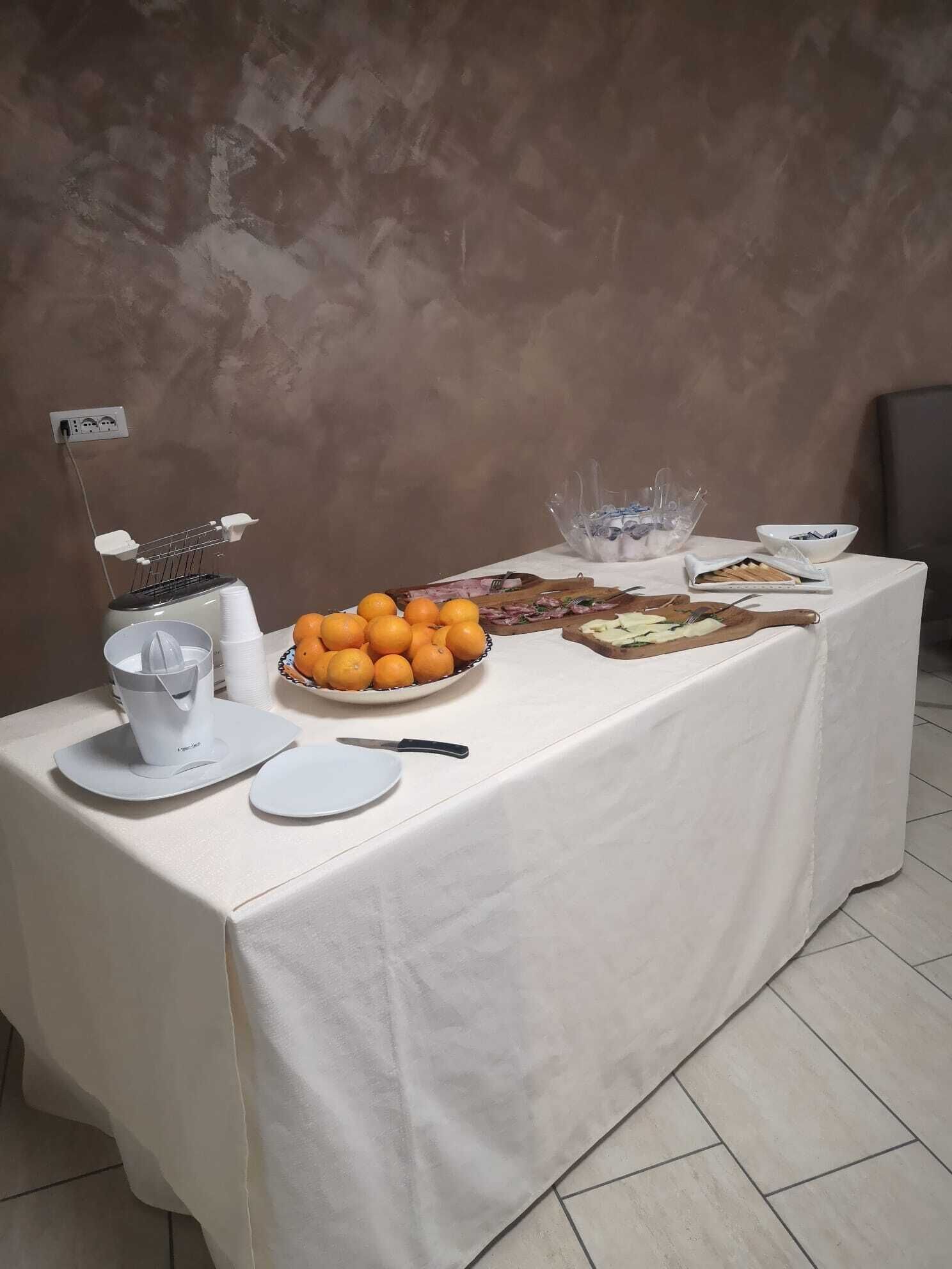 Una mesa dispuesta con un exprimidor, cuencos de naranjas, un cuchillo y una tabla de cortar con alimentos.