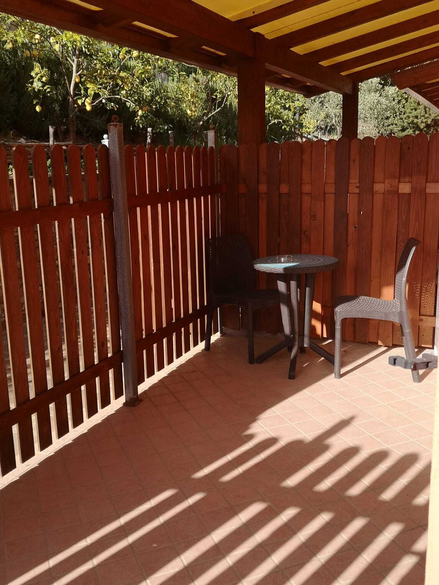 A patio with a wooden fence, a round table, two chairs, and a pergola overhead.
