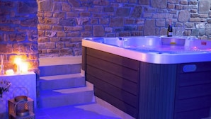 A hot tub with a stone wall backdrop, a bottle of champagne, and glasses on a table. - Cilento Holiday Village (Montecorice)