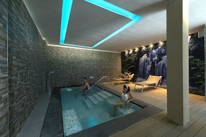 A modern indoor pool area with a waterfall mural, lounge chairs, and a stone-tiled wall. - Hotel Paradiso Terme (Abano Terme)