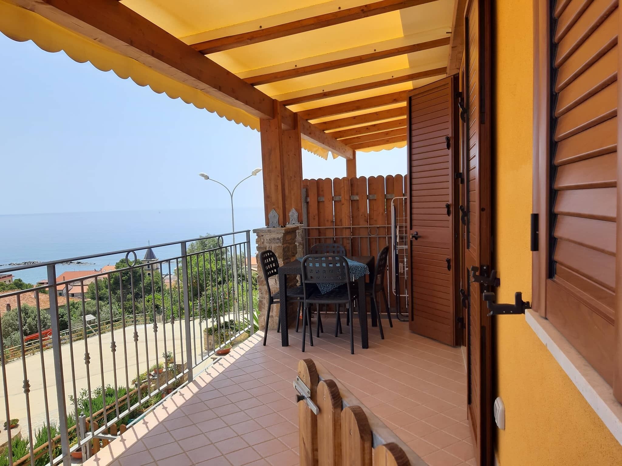 Un balcone con una pergola in legno, un tavolo con sedie e vista sul mare.