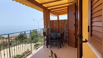 Un balcone con una pergola in legno, un tavolo con sedie e vista sul mare.