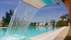 Piscina con elemento d'acqua, acqua cristallina e area solarium piastrellata.
