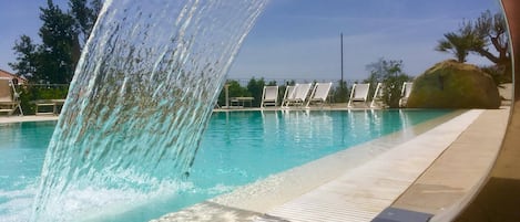 A swimming pool with a water feature, clear blue water, and a tiled deck area.