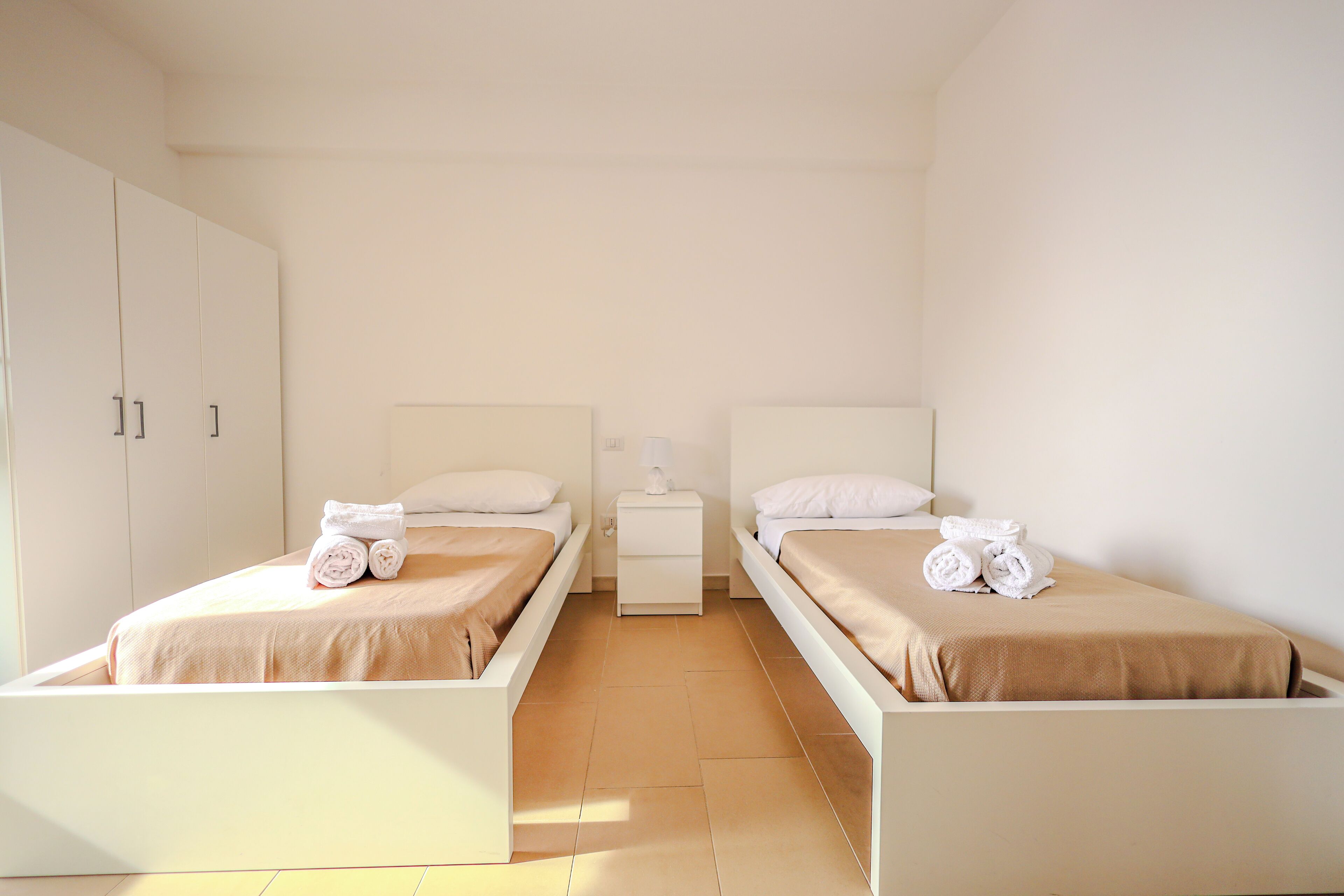 A hotel room with two single beds, a nightstand, and a wardrobe.
