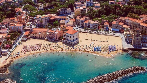 Una vista aerea di una cittadina costiera con spiaggia, edifici e acque blu cristalline.
