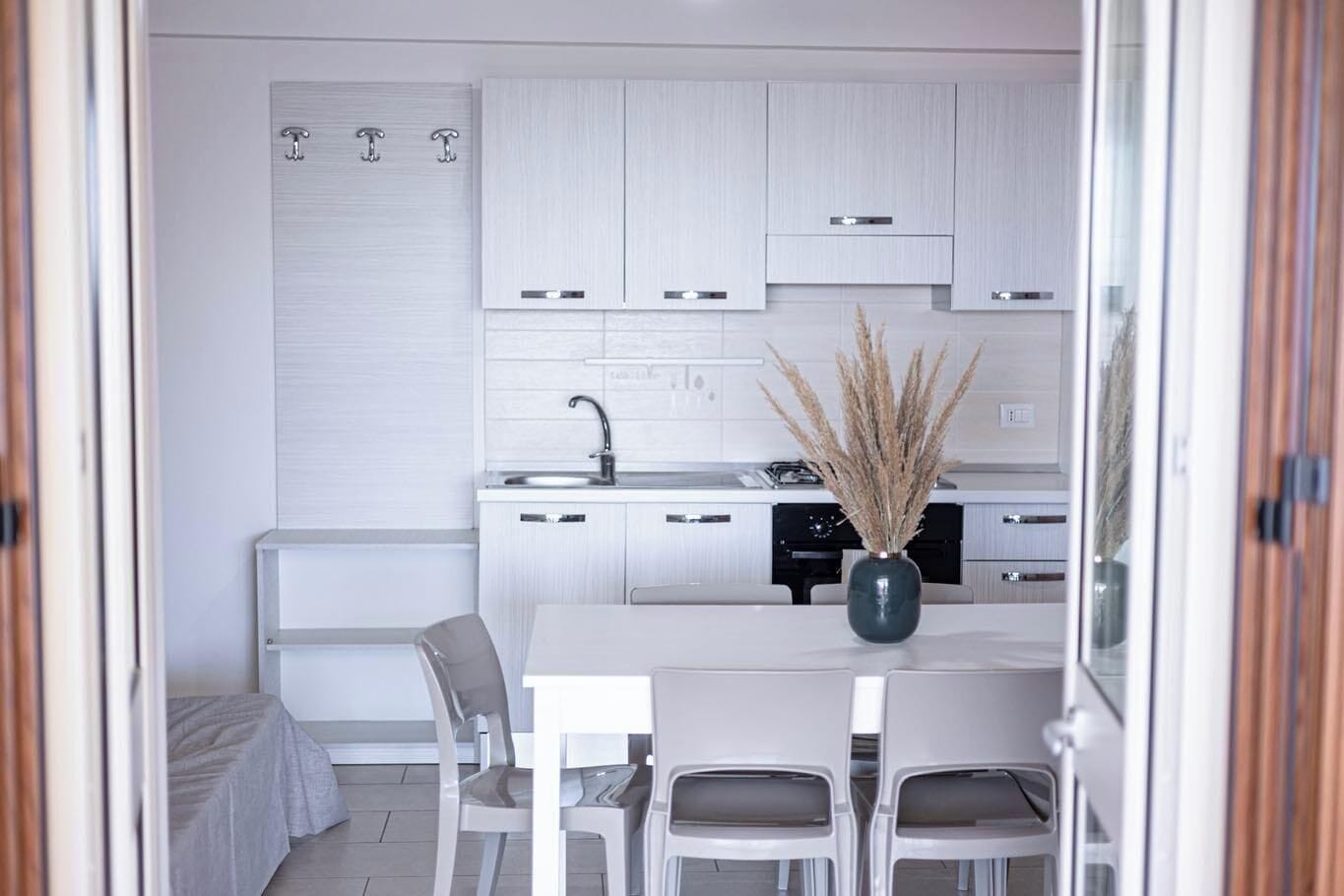 A modern kitchen with white cabinetry, a central island with chairs, and a vase of dried plants.
