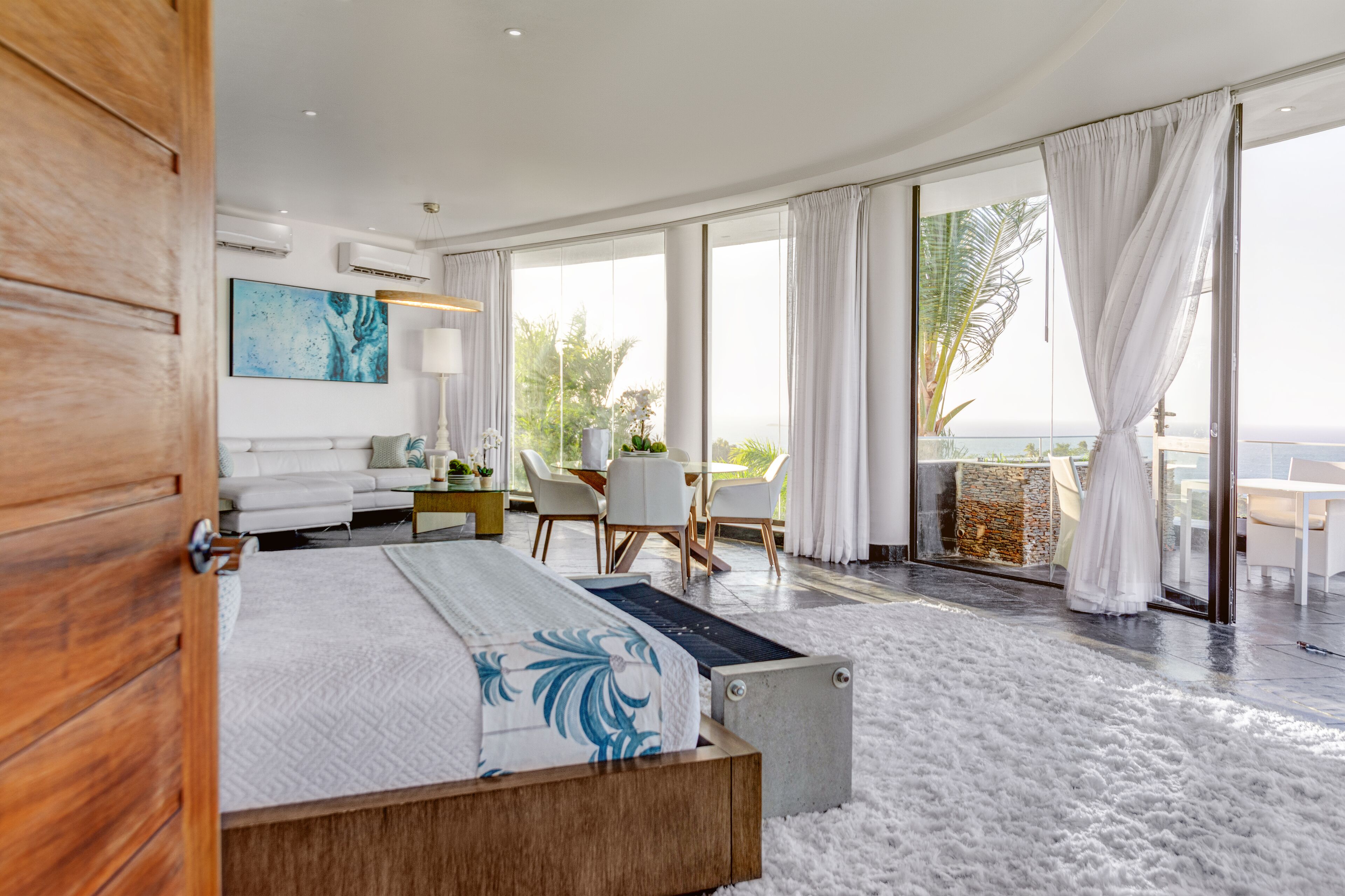 A modern bedroom with a large bed, a desk, and a view of the ocean.