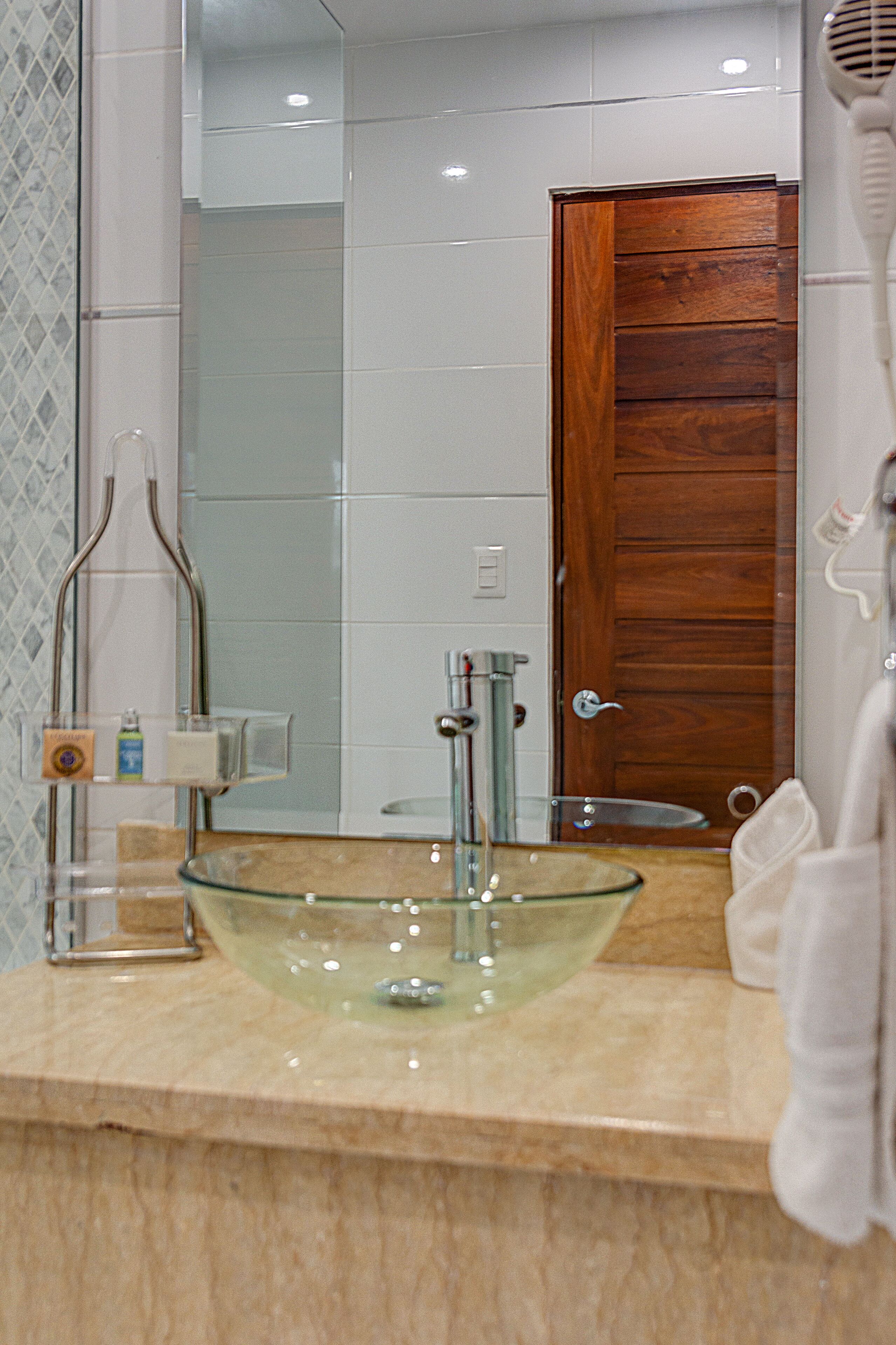 A bathroom with a glass bowl sink, a wooden door, and a towel rack.