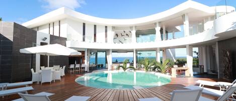 A modern resort with a central pool, outdoor seating, and a view of the ocean.