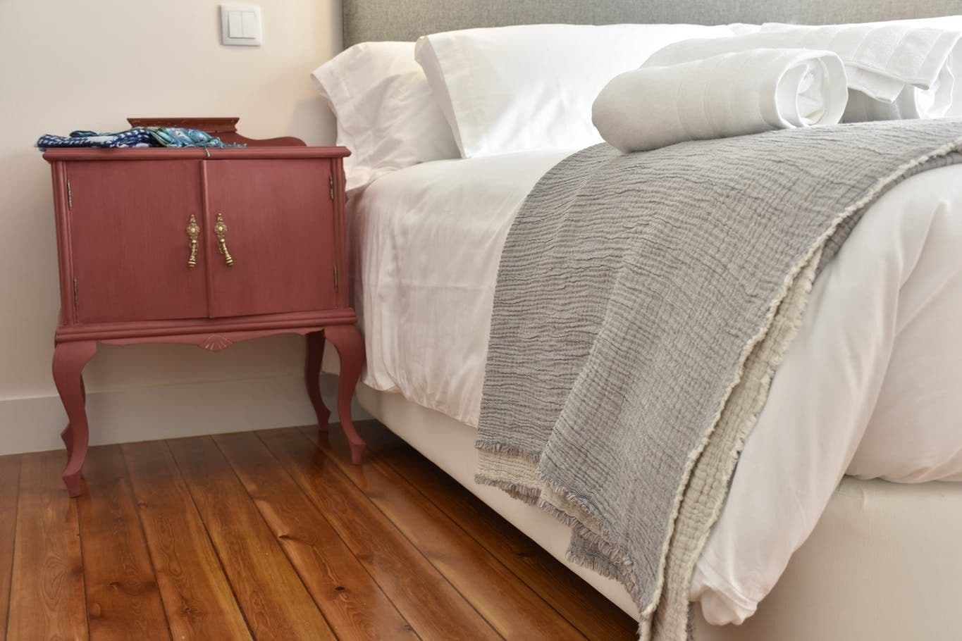 Un dormitorio con cama, mesita de noche de madera y manta gris.