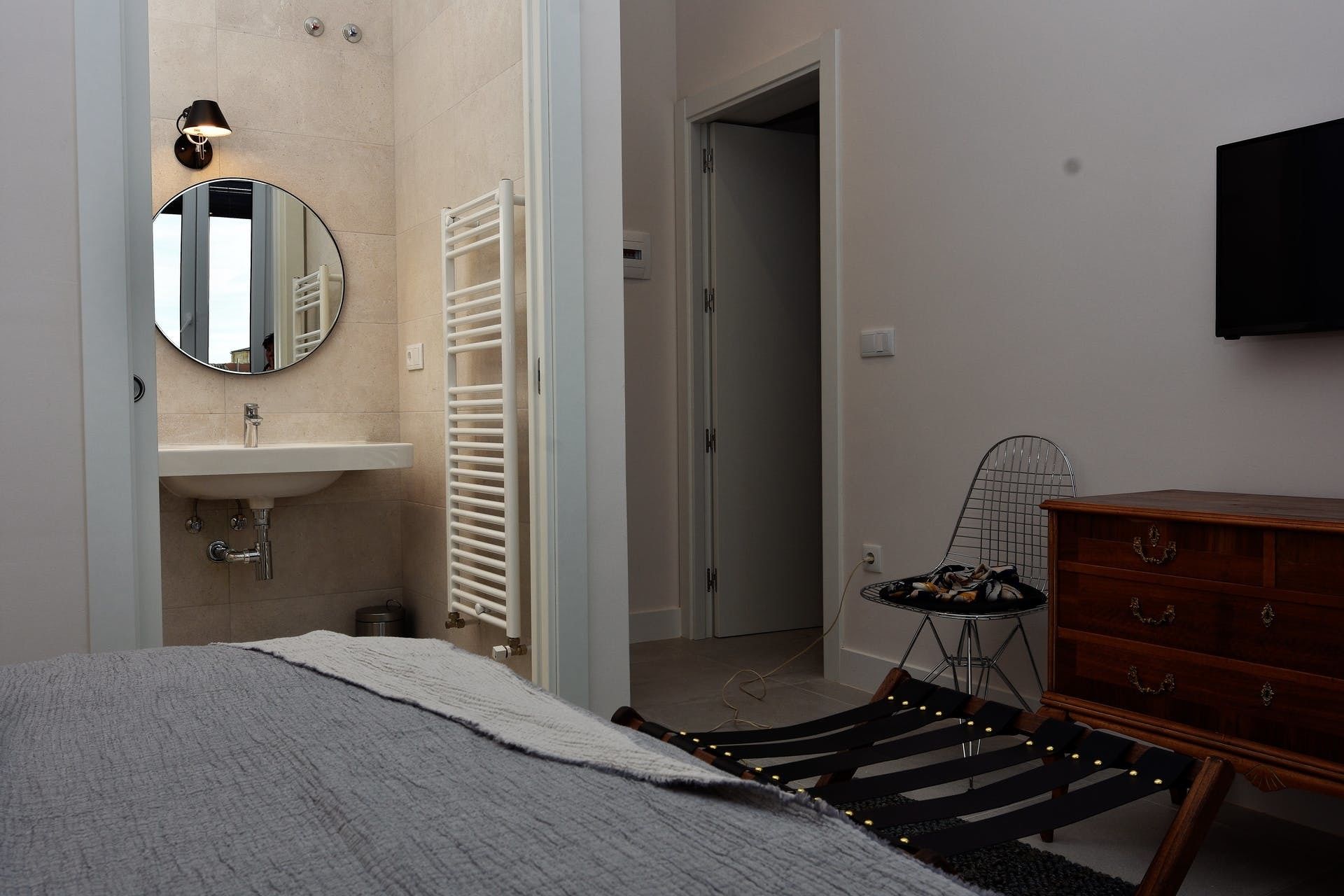 Un dormitorio con cama, cómoda, espejo, radiador, lavabo y televisor.