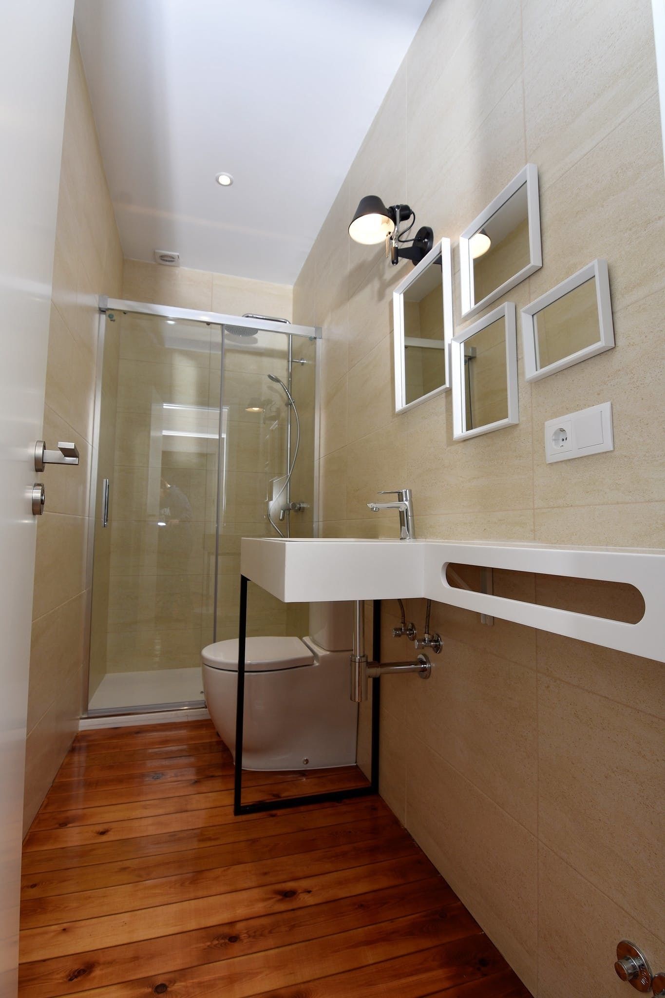 Un baño moderno con cabina de ducha de vidrio, un lavabo blanco con encimera curvada y un espejo con tres espejos rectangulares encima.