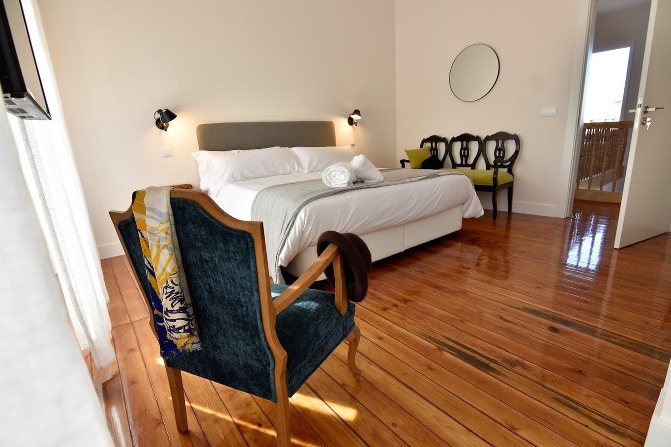 A bedroom with a bed, two chairs, a mirror, and a wooden floor.