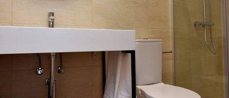 A bathroom with a wooden floor, a white sink, a round mirror, a toilet, and a glass shower enclosure.
