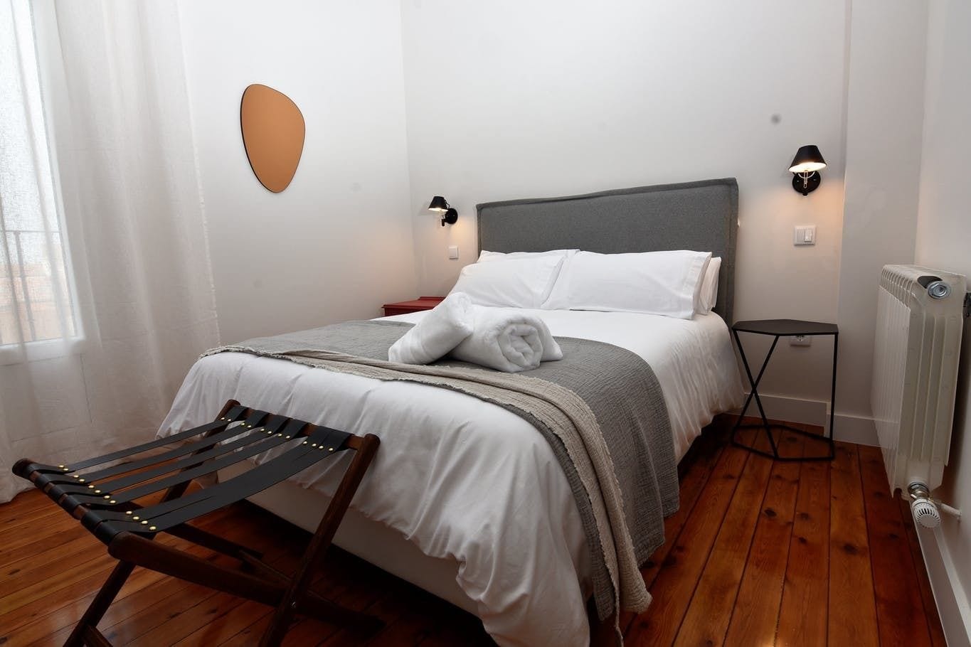 A neatly made bed with white linens, a grey headboard, and two bedside lamps.