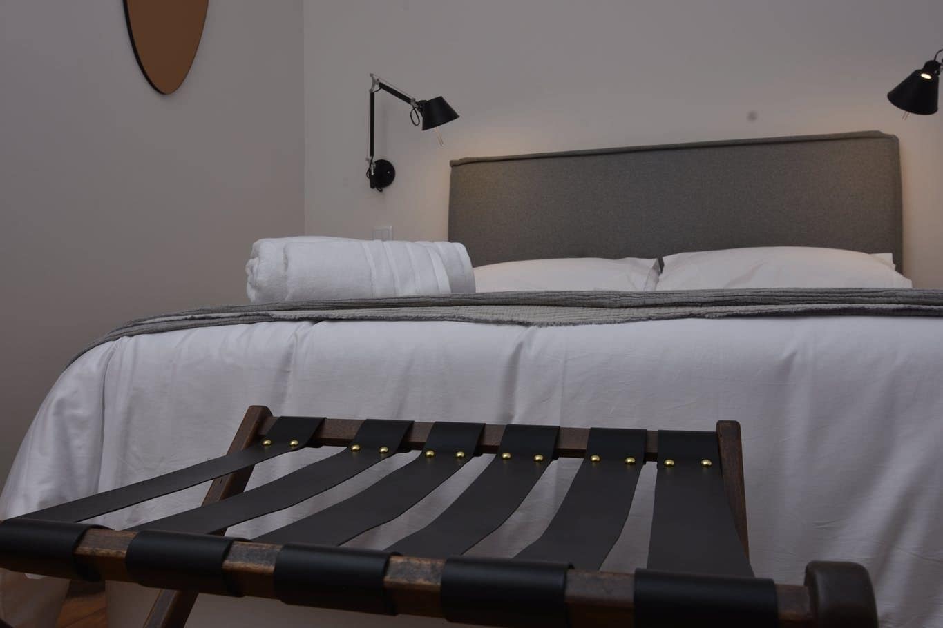 Una cama bien hecha con sábanas blancas, un cabecero gris y dos lámparas de noche.
