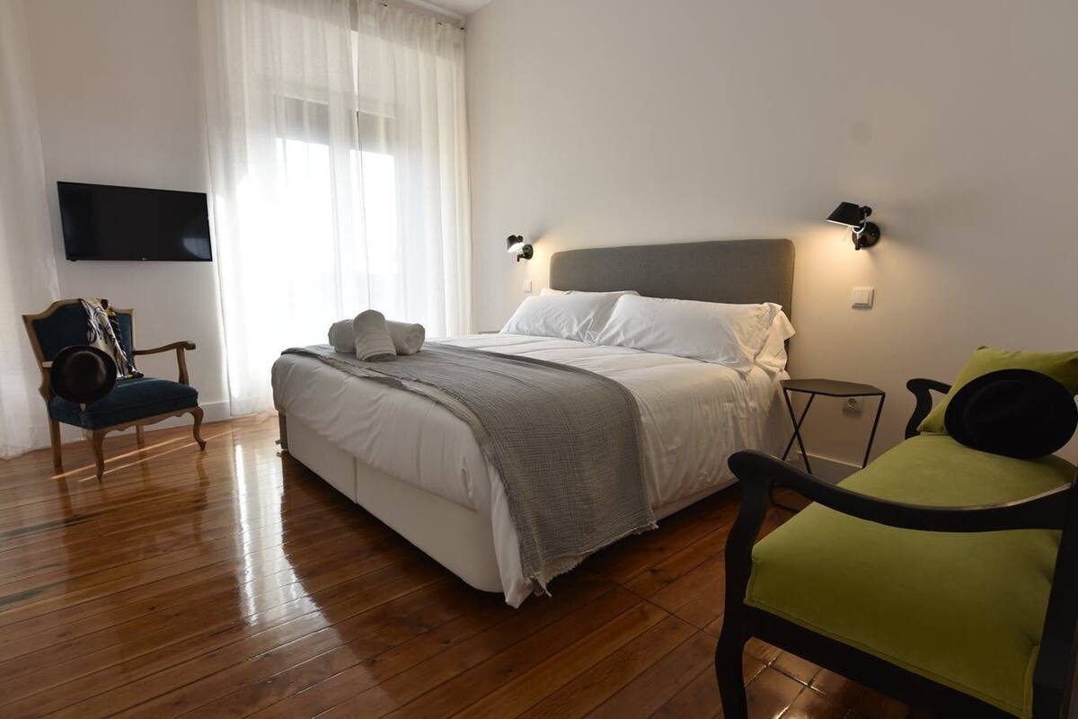 Een slaapkamer met een bed, een stoel, een televisie en een wandlamp.