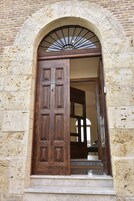 Una puerta de madera con un tragaluz metálico encima, en una pared de piedra.
