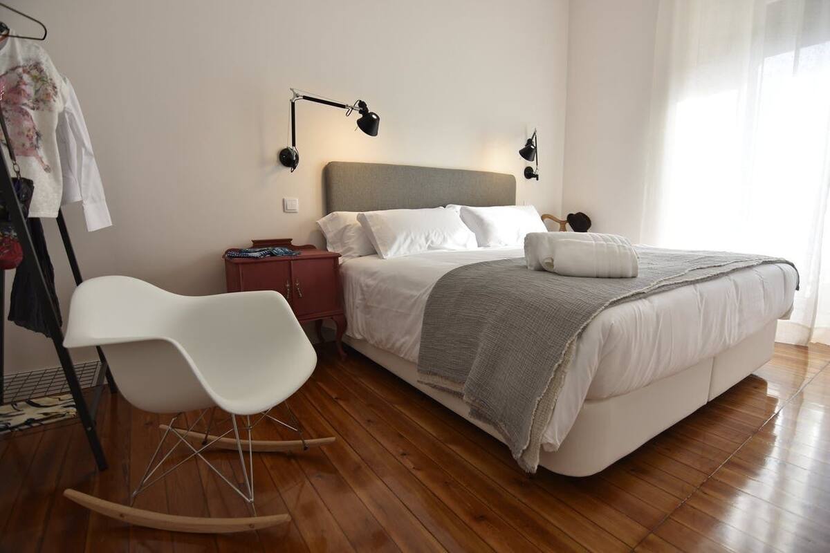 Een slaapkamer met een bed, een schommelstoel, een nachtkastje en een wandlamp.