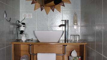 A bathroom with a wooden vanity, a white sink, a mirror with a sunburst frame, a towel rack, and a trash can.