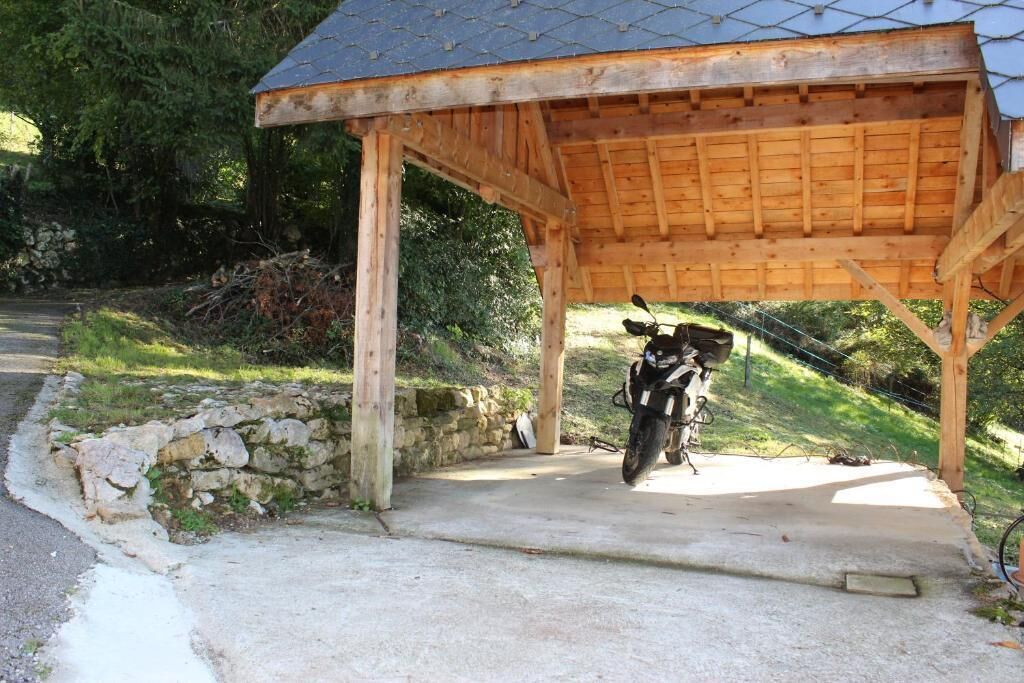 Un espace extérieur abrité où une moto est garée sous un abri en bois.