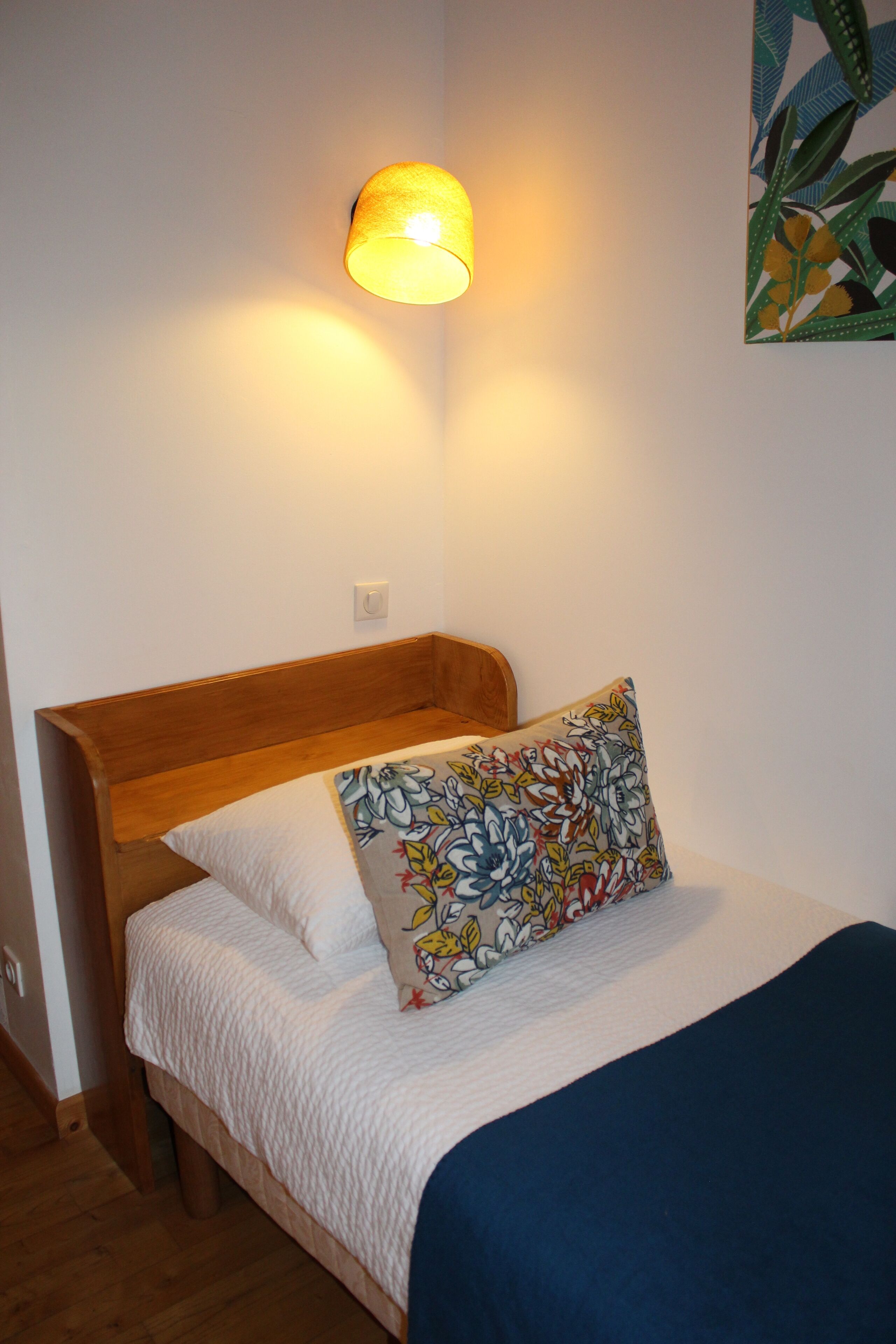 Un lit simple avec une tête de lit en bois, un oreiller blanc, un oreiller coloré et une couverture bleue.